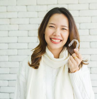 Woman in white sweater holding an Invisalign aligner