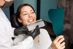 Woman holding hand mirror to see shade guide being held to her teeth